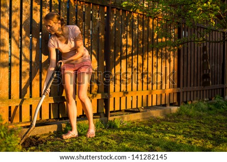 Pretty female gardener taking care of her lovely garden on a lovely spring day - cutting branches, double digging/loosening the soil with a spade