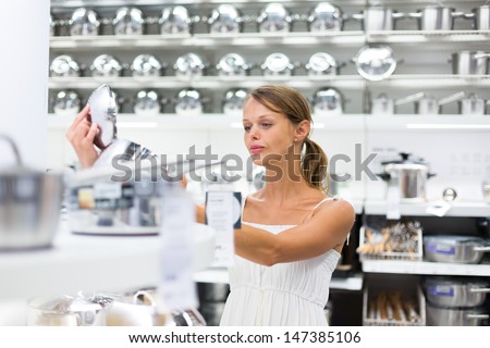 Pretty, young woman choosing a the right pot for her cooking in a modern home furnishings store (color toned image; shallow DOF)