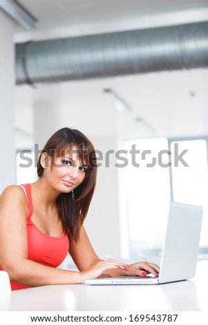 Pretty young woman working on her laptop in an office/university study room/library