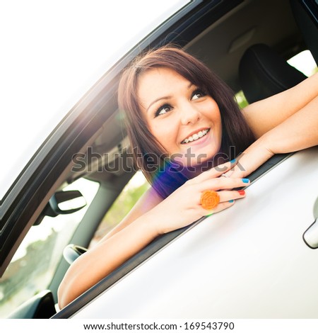 Cute, happy young female driver on a lovely day looking out of the window of her brand new car (color toned image)