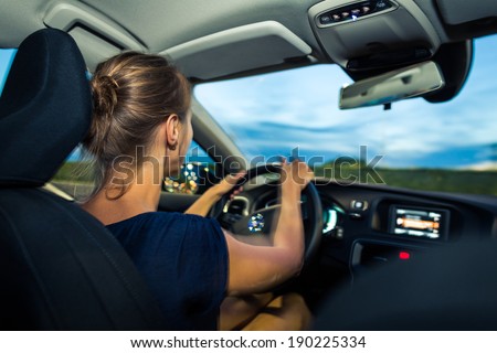 Young, woman driving a car at dusk, going home from work (long exposure used -> slighlty motion blurred image - give sense of speed/movement)