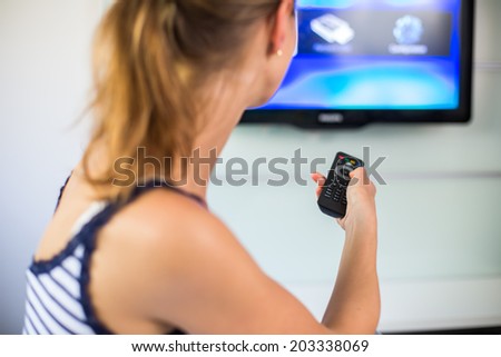 Young woman at home watching TV, turning it on, changing channels