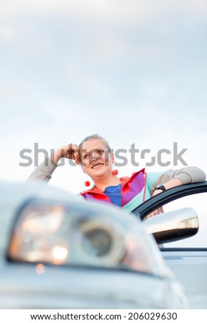Portrait of a cheerful female teen driver, by her new car, looking very happy