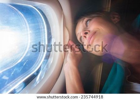 Happy, female airplane passanger enjoying the view from the cabin window over the blue sky (shallow DOF; intentional flare)