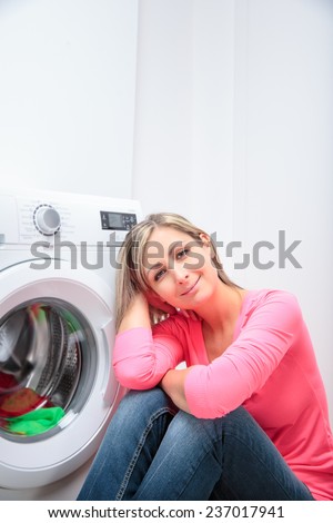 Housework: young woman doing laundry - waiting for the washing program to end - impatient to have her clothes washed, dry and ready to wear (shallow DOF; color toned image)