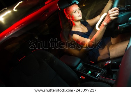 Driving a car at night - pretty, young woman driving her modern car at night, in a city (shallow DOF; color toned image)