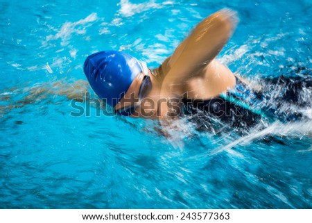 Female swimmer in an indoor swimming pool - doing crawl (shallow DOF; motion blur technique used to convey fast movement of the swimmer)