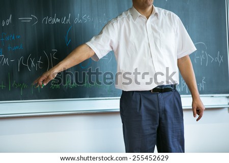 teacher teaching mathematics while pointing at blackboard in classroom