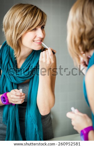 Pretty, young woman applying mascara /eyeshadows in front of a mirror