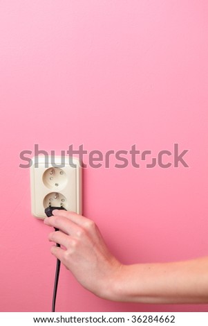 Young woman\'s hand plugging a power plug into an electric wall socket at a pink wall