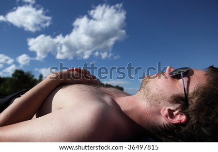 Young man lying on a beach, sunbathing under lovely summer sky
