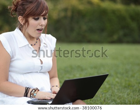 Surprised - pretty young woman working on a laptop computer outdoors seeing something that surprises her