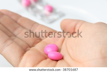 Taking pills/taking painkillers - hand holding two pills/tablets isolated on white with some more pills in the background