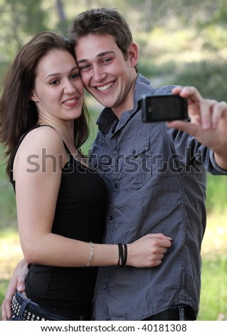 Beautiful young caucasian couple having fun while taking autoportrait pictures of themselves outdoors in a park