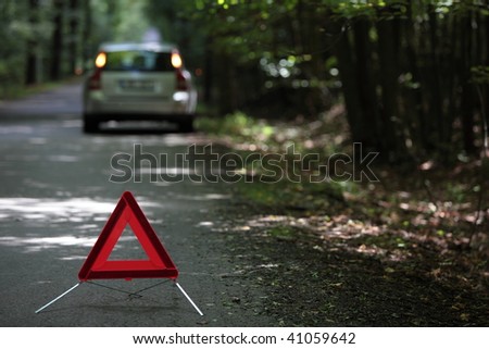broken down car with warning triangle behind it waiting for assistance to arrive (shallow depth of field, the focus is on the triangle, the car is out of focus)