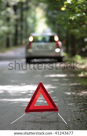 broken down car with warning triangle behind it waiting for assistance to arrive (shallow depth of field, the focus is on the triangle, the car is left out of focus)