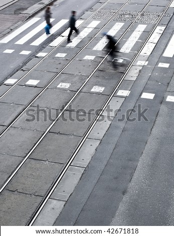 urban traffic concept - city street with a crossing, rail, motion blurred cyclist and pedestrians (color toned image)