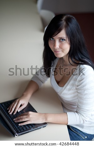 pretty young brunette working/typing on a laptop computer in a office/classroom