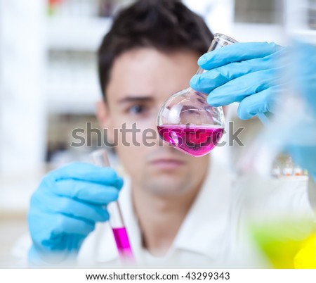 close-up portrait of a young male researcher carrying out experiments in a research lab (focus on the retort, the man is intentionally left out of focus)