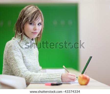 portrait of a pretty young blonde college student smiling while taking notes in a her college major class