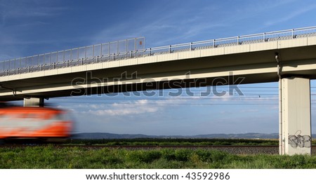 fast train going really fast through a lovely summer landscape and under a highway bridge