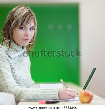 Portrait of a pretty young blonde college student smiling while taking notes in a her college major class