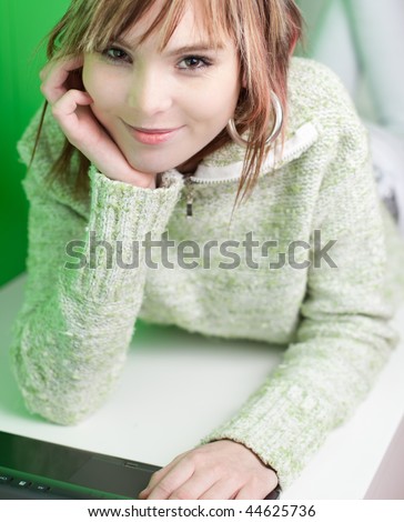 pretty young college student working on her laptop computer in front of a green wall (looking at you)