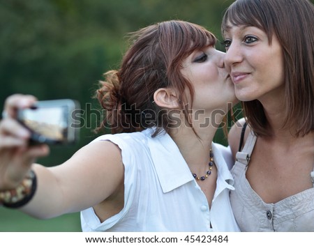 two young caucasian female friends taking autoportraits of themselves kissing, having fun