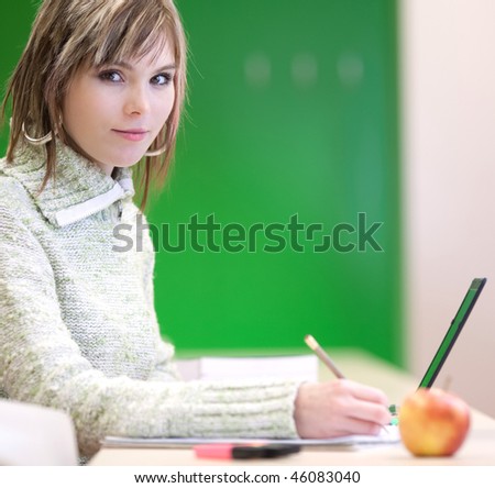 Portrait of a pretty young blonde lefty college student smiling while taking notes in a her college major class  (