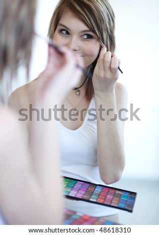 pretty young woman applying mascara /eyeshadows in front of a mirror