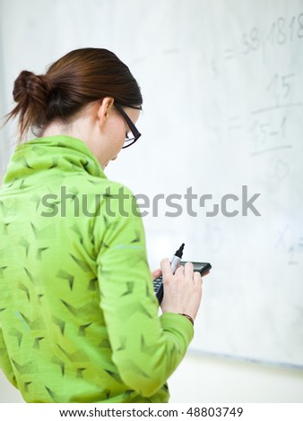 young female college student in front of a whiteboard using a calculator during math class