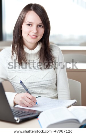 portrait of a pretty young brunette college student working in a classroom