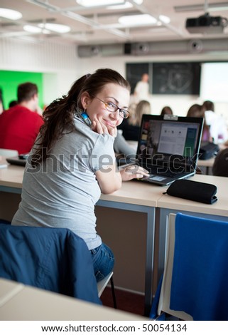 young pretty female college student sitting in a classroom full of students during class