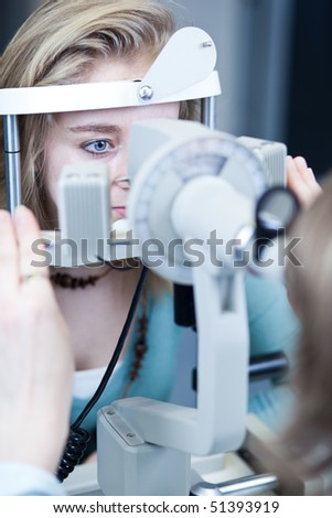 optometry concept - pretty young woman having her eyes examined by an eye doctor (color toned image)