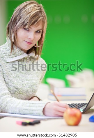 Portrait of a pretty young blond college student smiling while taking notes in a her college major class
