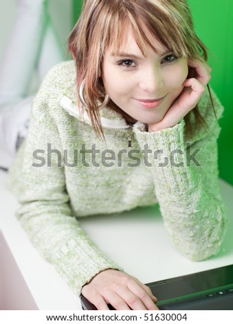 Portrait of a pretty young college student working on her laptop computer in front of a green wall (looking at you)