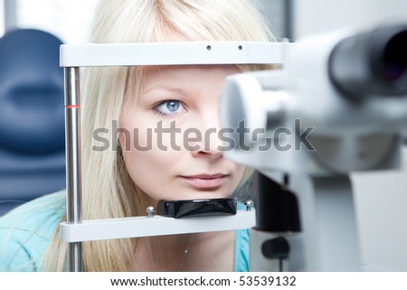 optometry concept - pretty young woman having her eyes examined by an eye doctor on a slit lamp