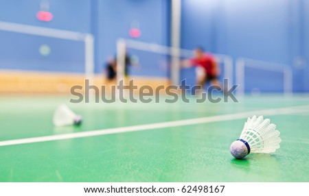 badminton - indoor badminton courts with players; shallow DOF, sharp focus on the shuttlecock in the foreground (color toned image)