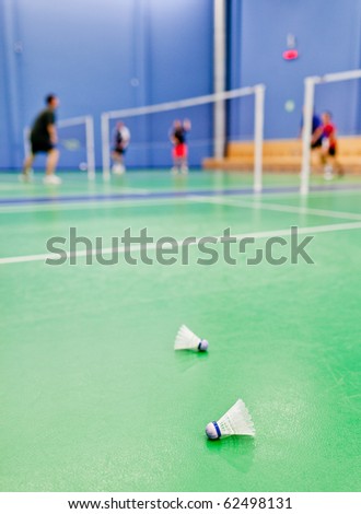 badminton - indoor badminton courts with players; shallow DOF, sharp focus on the shuttlecock in the foreground (color toned image)