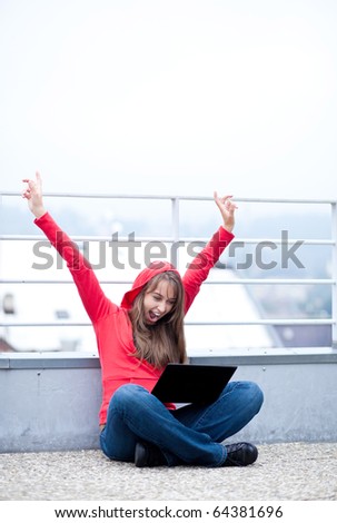 pretty young female caucasian woman super excited/hilarious/elated about something she sees on her laptop computer while sitting on a rooftop