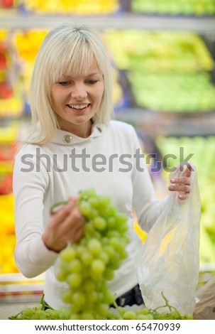 Beautiful young blonde woman shopping for fruits and vegetables in produce department of a grocery store/supermarket (shallow DOF; color toned image)