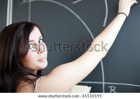 pretty, young teacher/college student drawing on the chalkboard/blackboard during a math class (shallow DOF; color toned image)