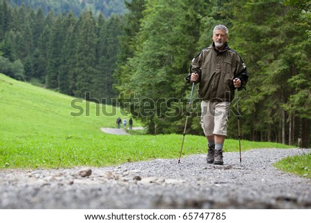 active handsome senior man nordic walking outdoors on a forest path, enjoying his retirement