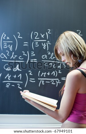 pretty young college student writing on the chalkboard/blackboard during a math class (shallow DOF; color toned image)