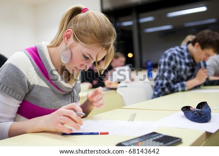 pretty female college student sitting an exam in a classroom full of students (shallow DOF; color toned image)
