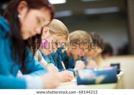 pretty female college student sitting an exam in a classroom full of students (shallow DOF; color toned image)