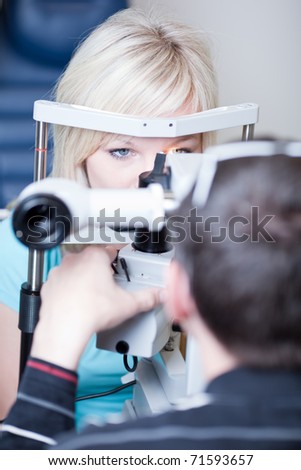 optometry concept - pretty young female patient having her eyes examined by an eye doctor (color toned image; shallow DOF)