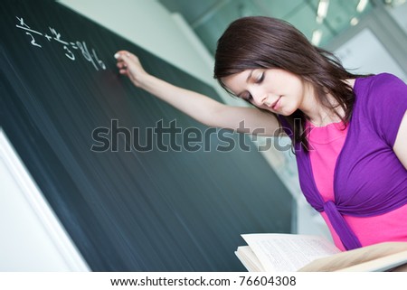 pretty, young college student writing on the chalkboard/blackboard during a math class (shallow DOF; color toned image)