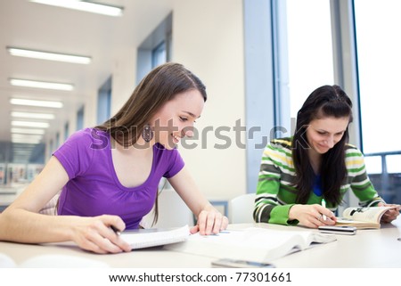 two pretty, young college students in a library (shallow DOF; color toned image)