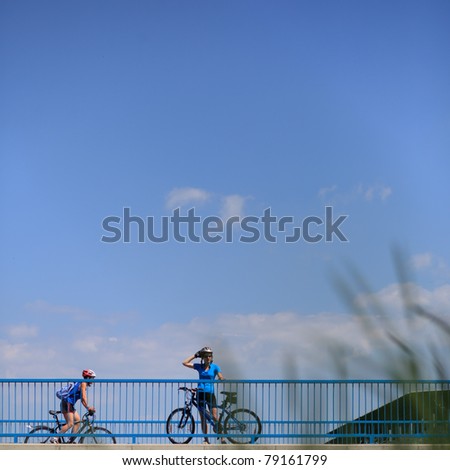 Background for poster or advertisment pertaining to cycling/sport/outdoor activities - female cyclist during a halt on a bridge against blue sky